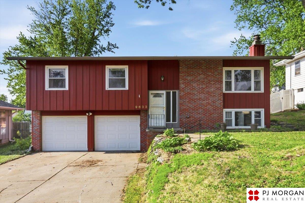 Red split-level house with brick accents, two garage doors, and a sloped front lawn.