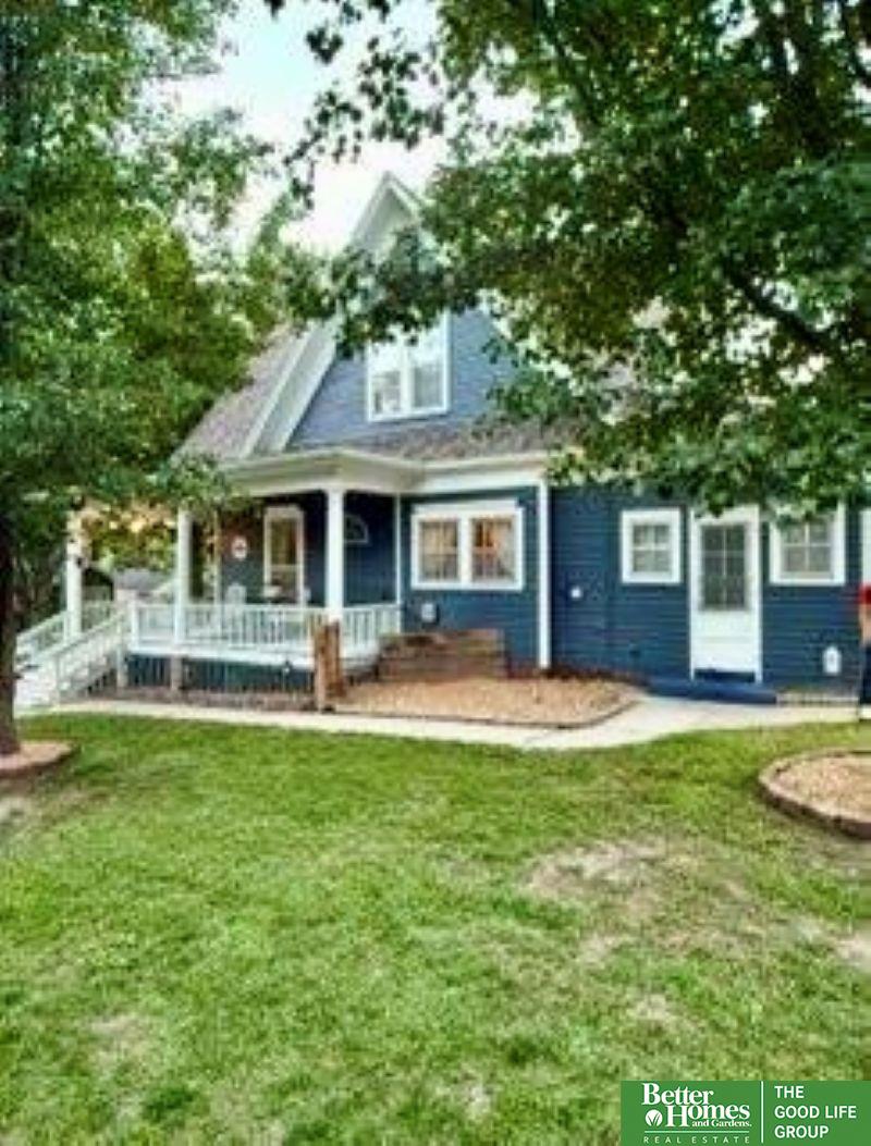 Blue two-story house with a covered porch, leafy trees, and a broad front lawn.