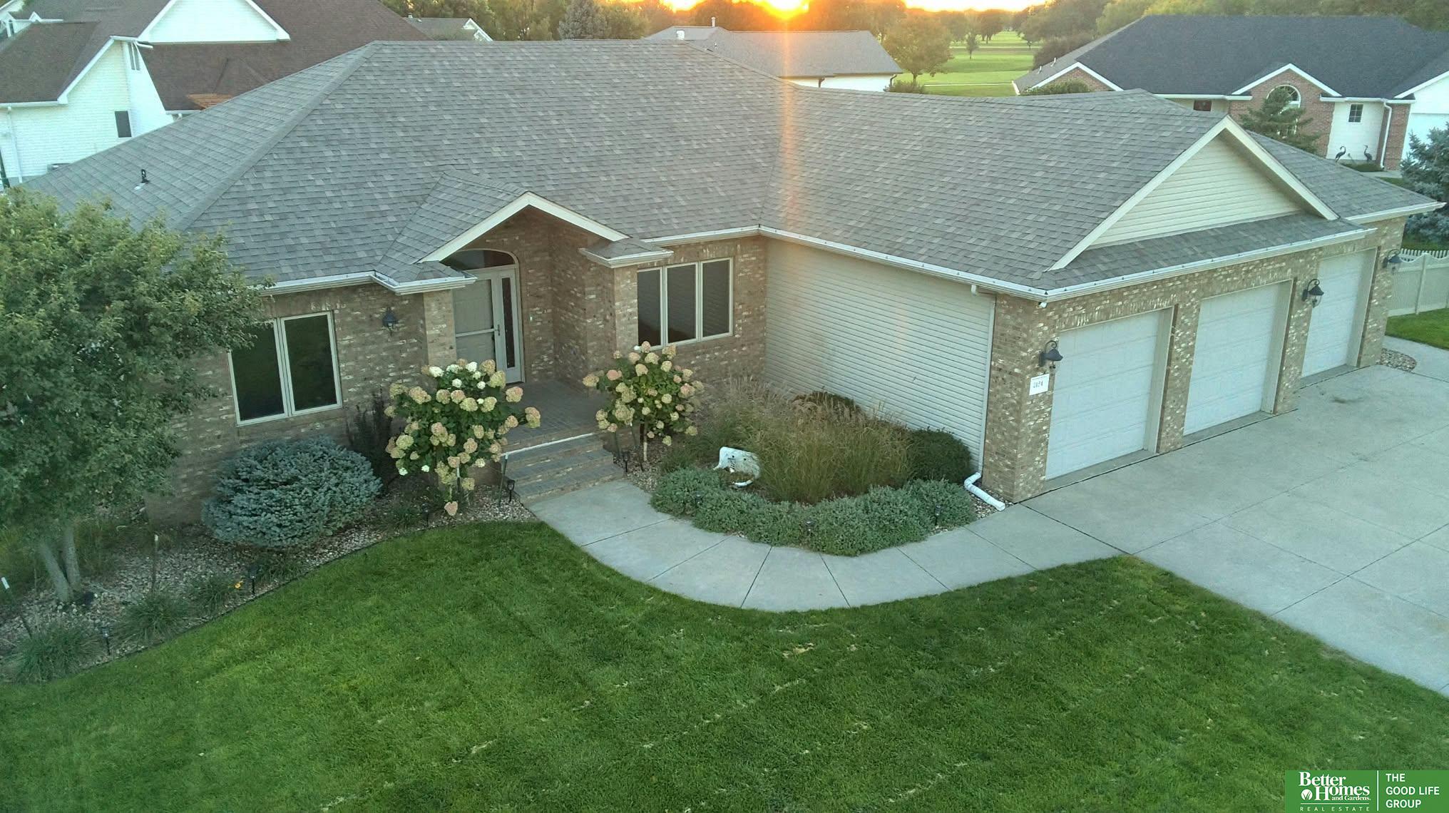 Brick-and-siding home with a three-car garage, landscaped entry, and curved walkway at sunset.