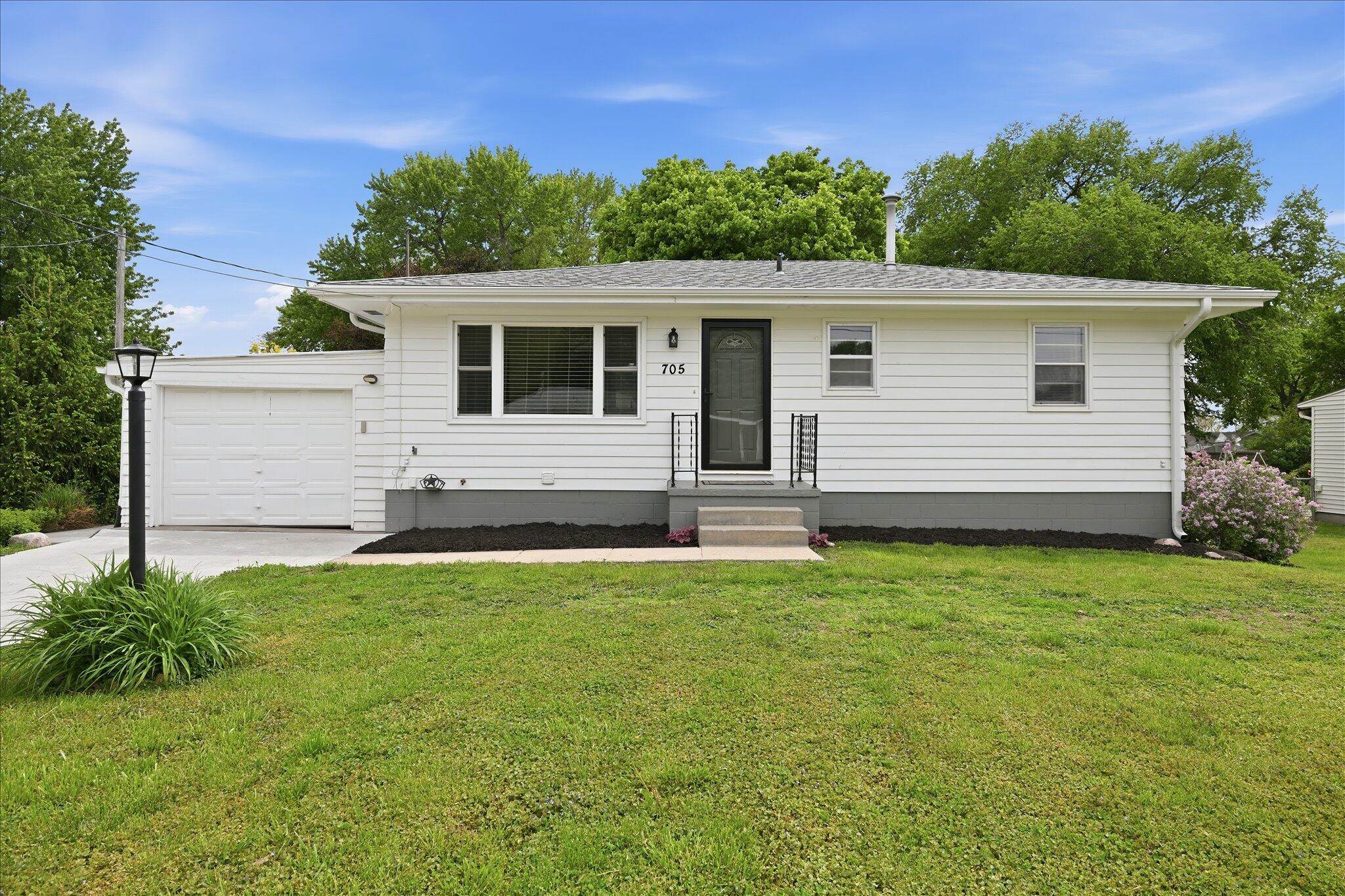 Single-story white house with an attached garage, dark front door, and broad green lawn.