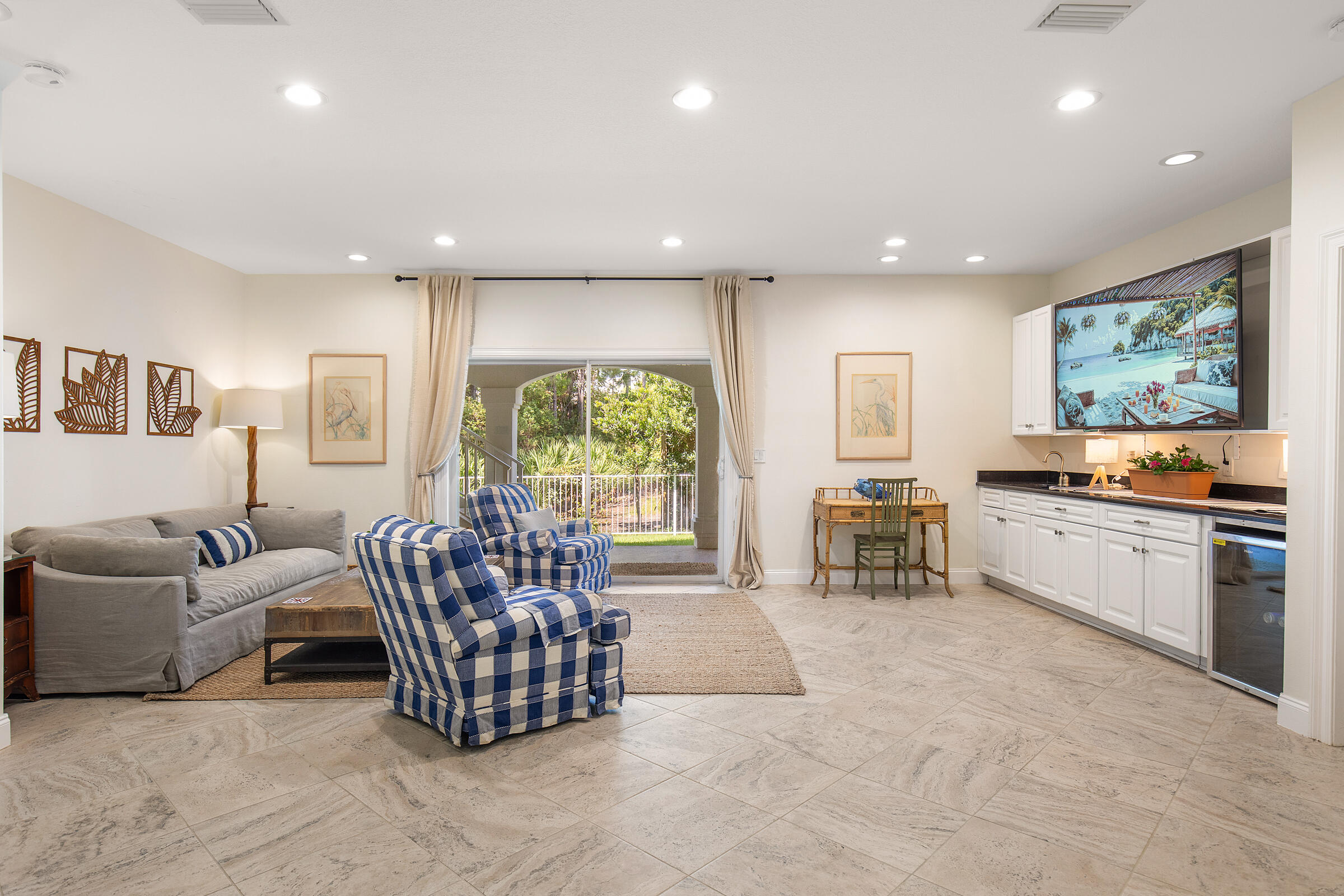 Furnished living room with checkered armchairs, a kitchenette, and sliding doors to a leafy patio.