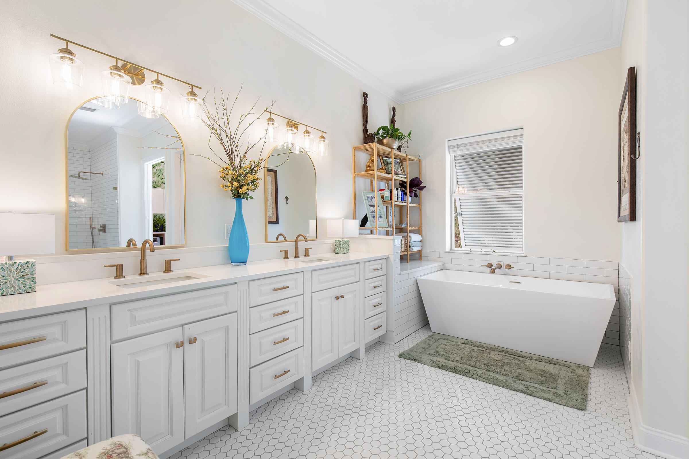 Bright bathroom with a white double vanity, arched mirrors, brass fixtures, and a freestanding soaking tub.