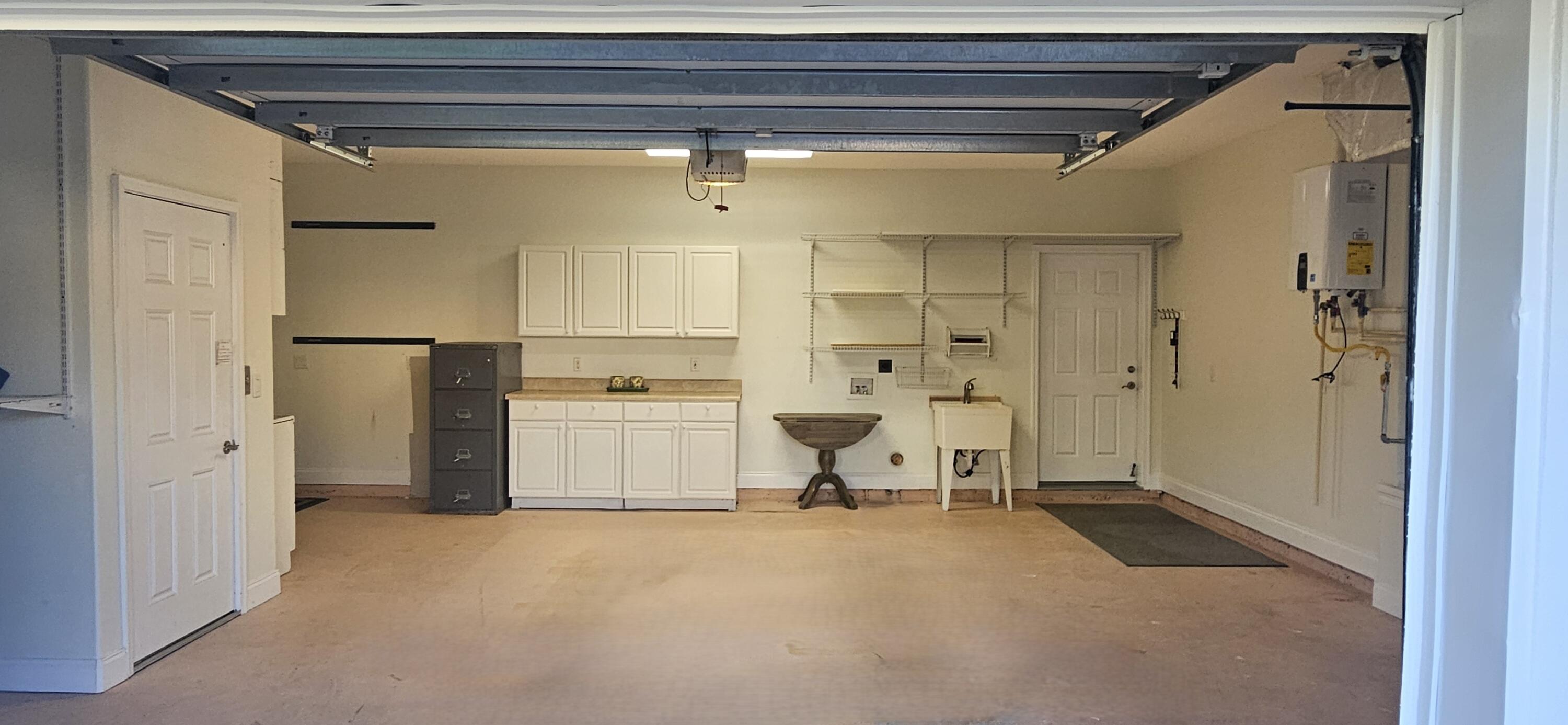 Empty garage with white storage cabinets, wall shelving, and a utility sink.