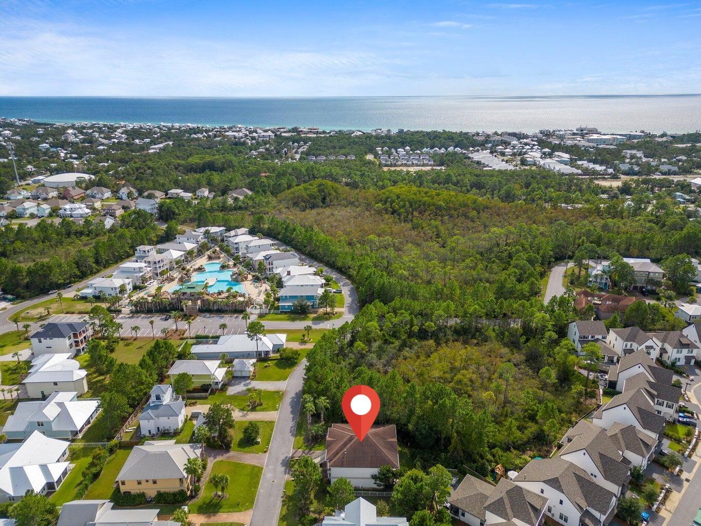 Aerial view of the property, neighborhood pool, wooded lots, and distant Gulf shoreline.