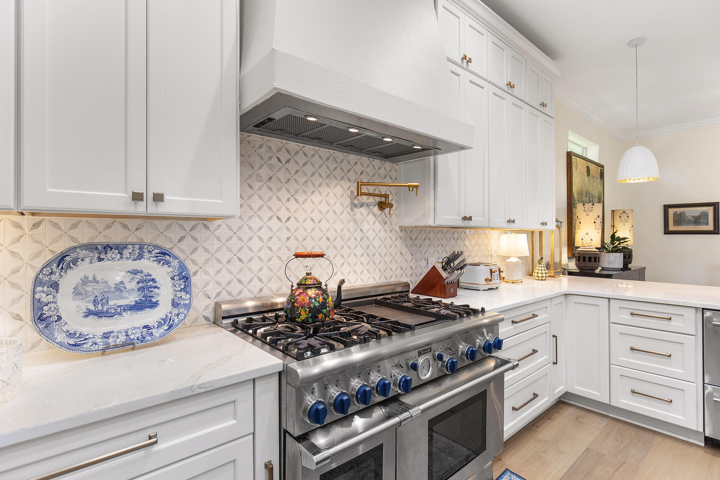 Kitchen with white cabinetry, geometric tile backsplash, and a large stainless steel range with blue knobs.