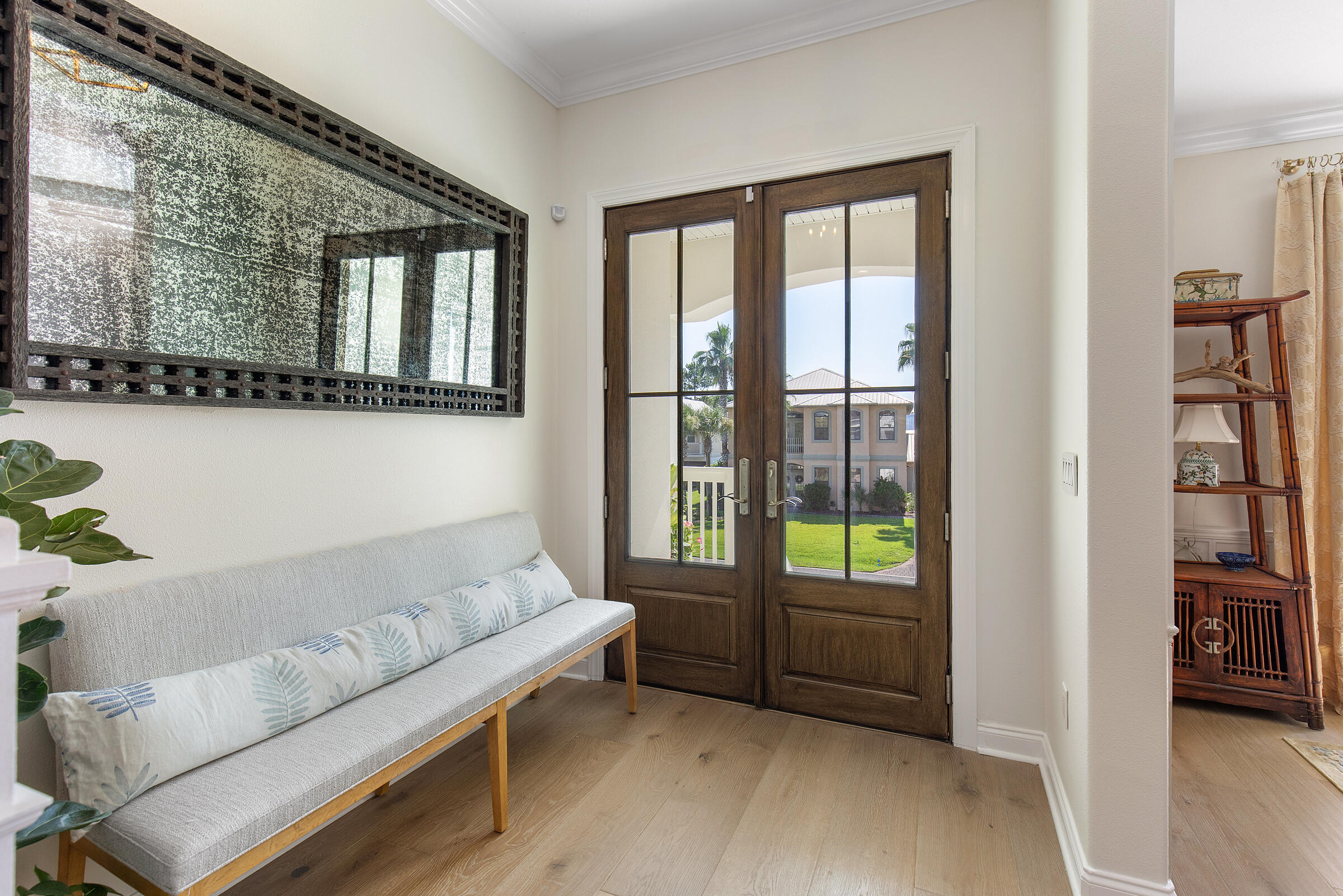 Entry foyer with an upholstered bench, large mirror, and glass-paneled double doors opening to a sunny lawn.