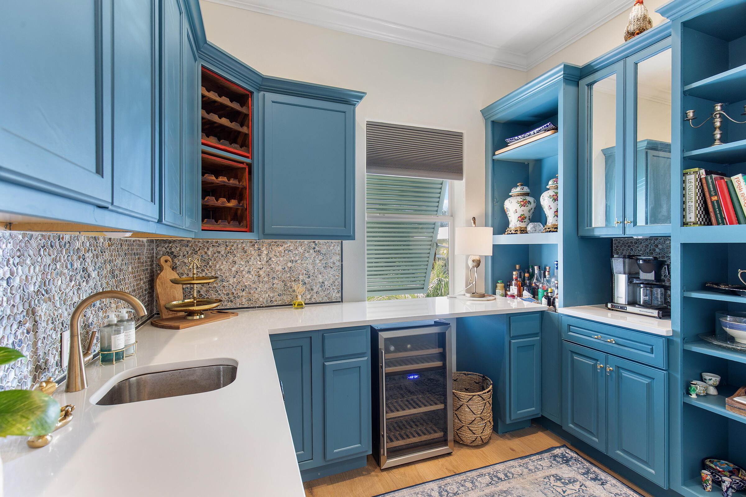 Blue kitchen with a white counter, sink, wine refrigerator, and patterned tile backsplash.