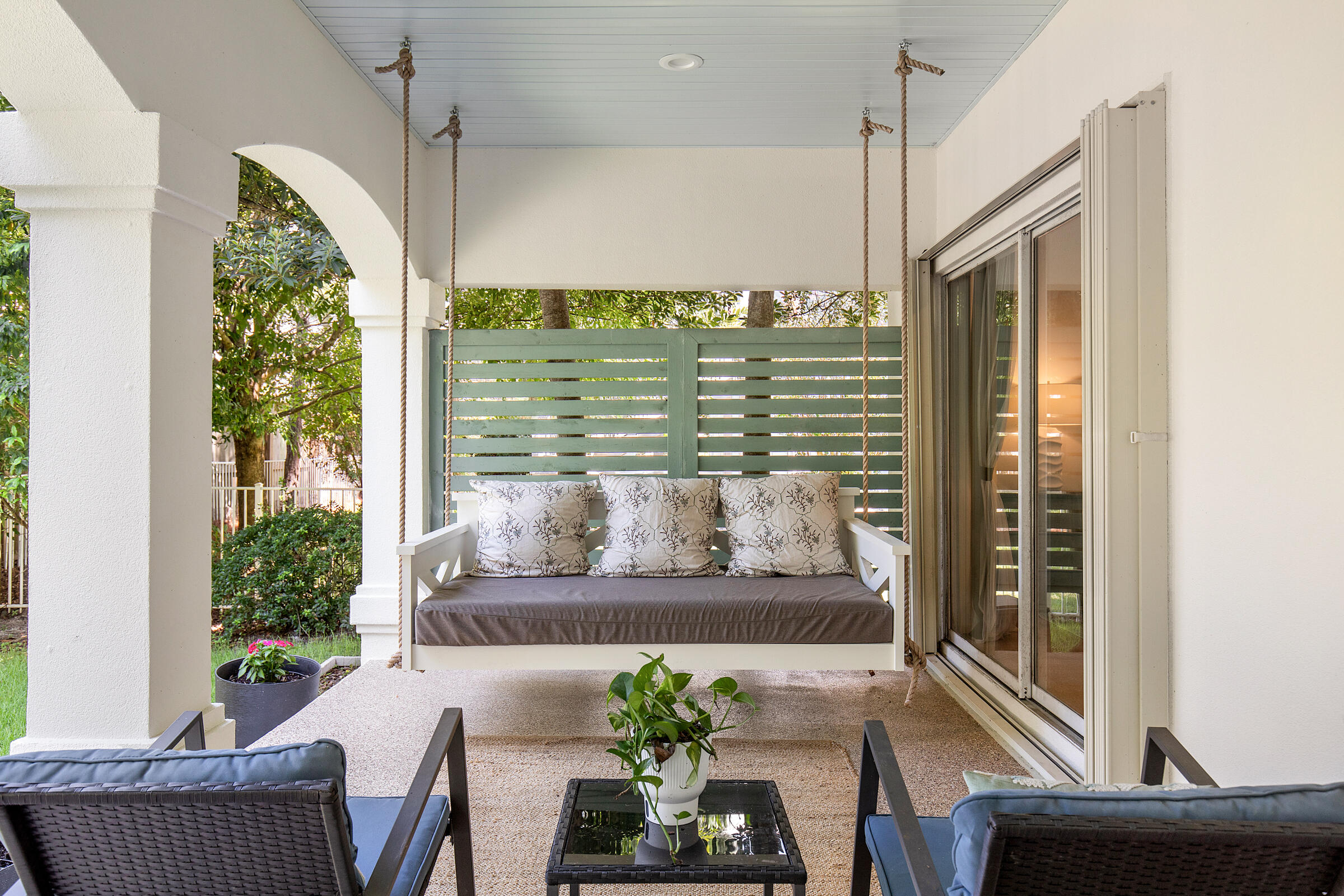 Covered patio with a cushioned hanging swing, lounge chairs, and sliding glass doors.