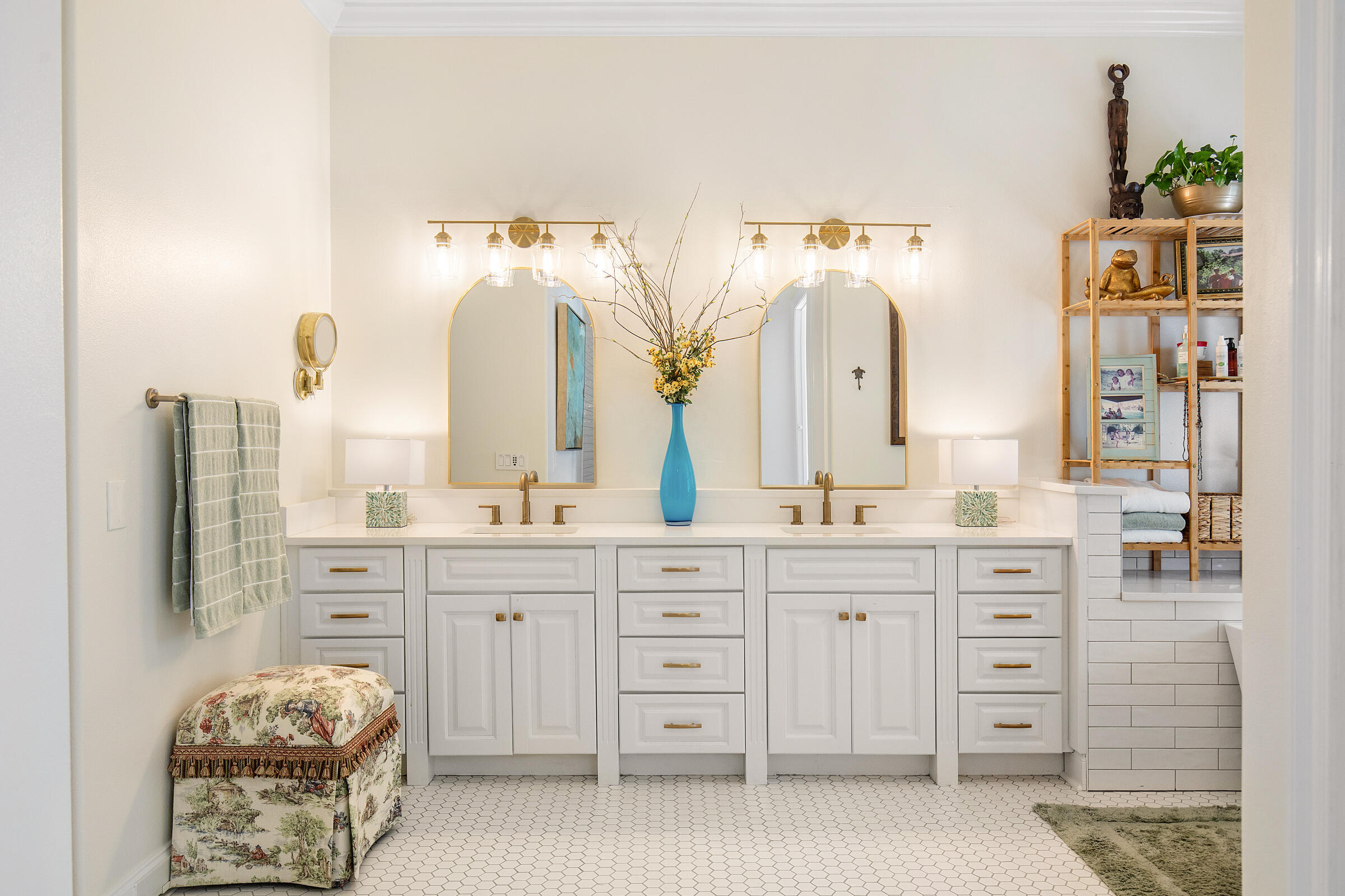 Bathroom with a white double vanity, arched mirrors, brass fixtures, and hexagonal floor tile.