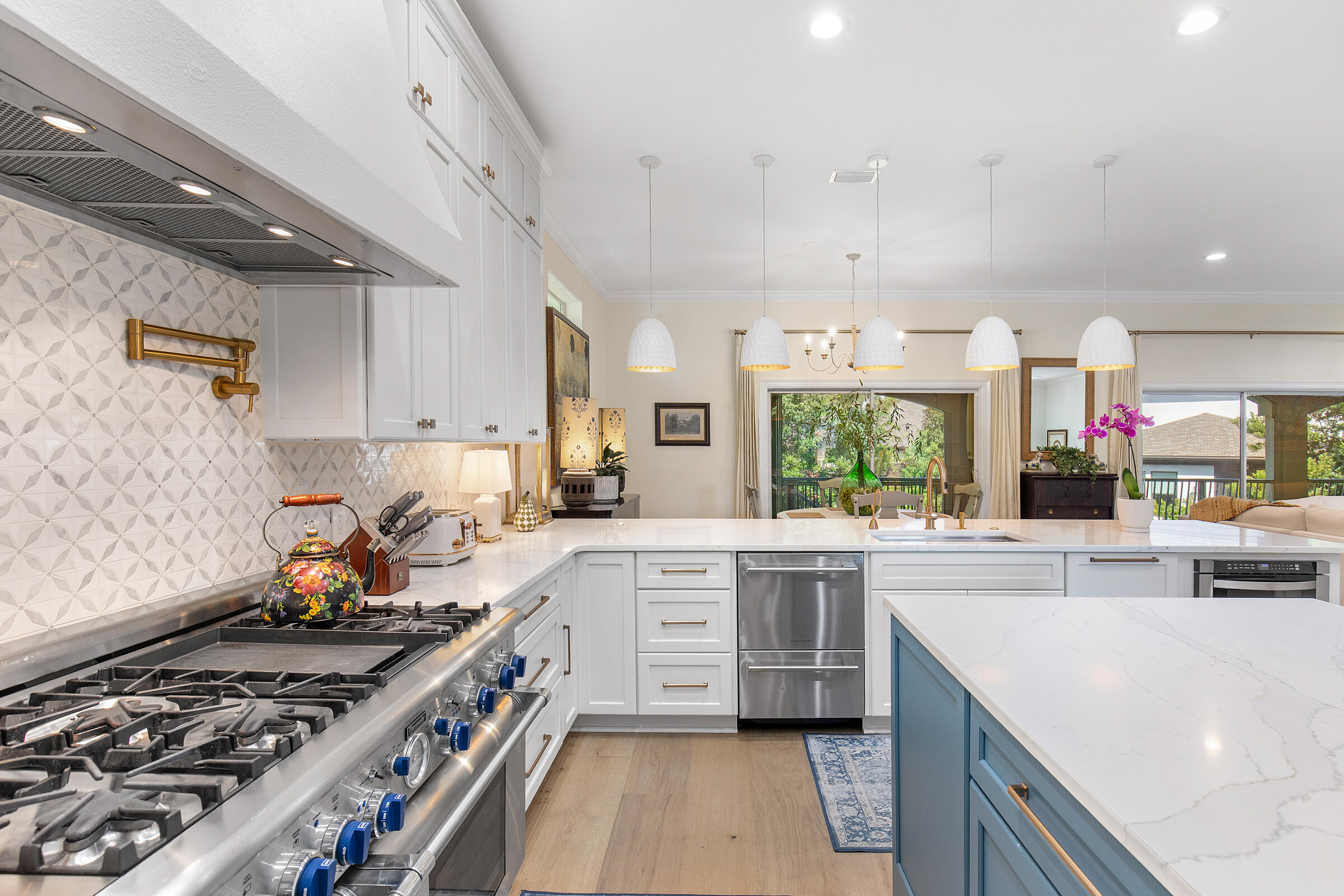 Bright kitchen with a blue island, white cabinetry, stainless steel range, and patterned backsplash.