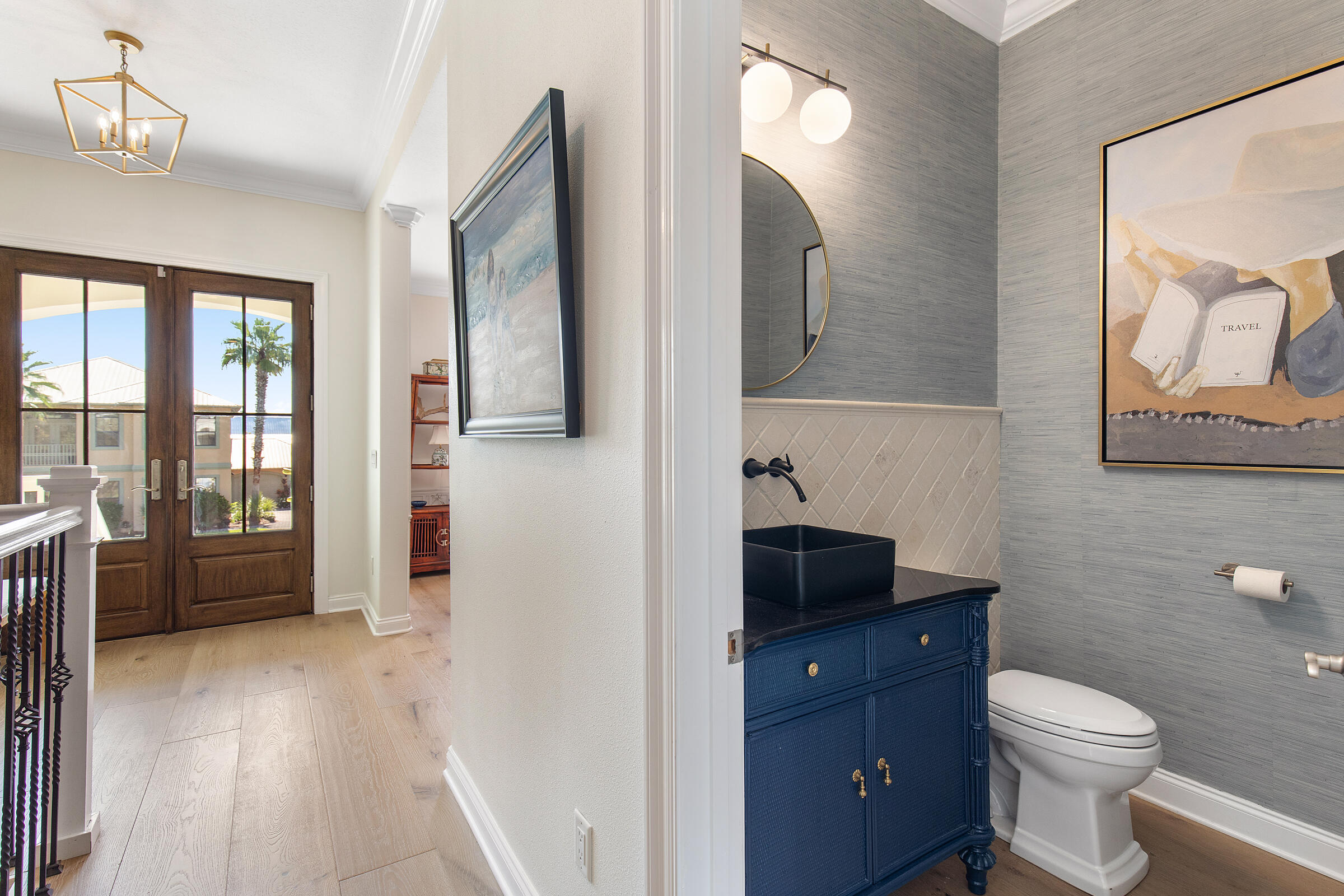 Powder room with a navy vanity and black vessel sink beside a bright hall with wood flooring.