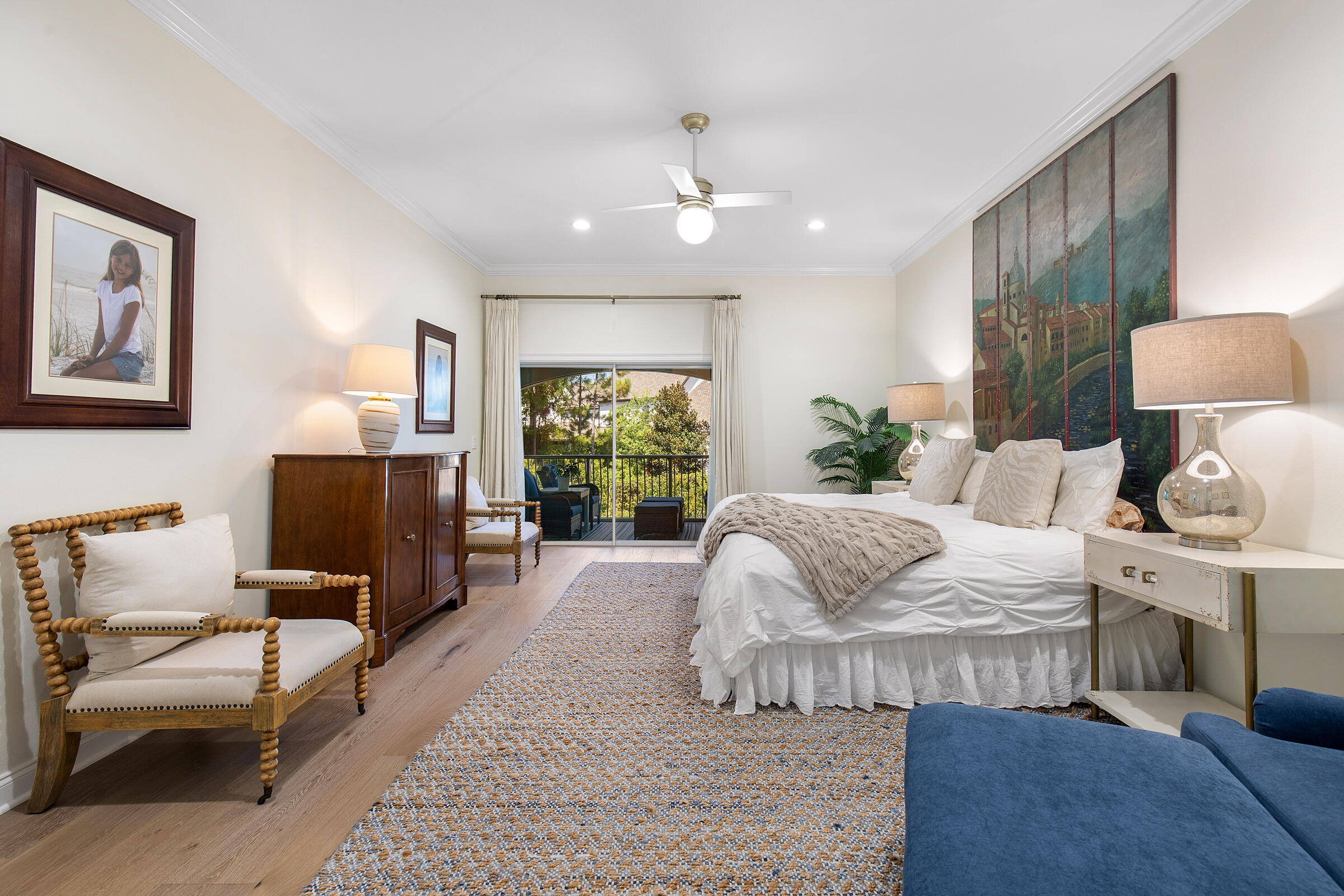 Bedroom with a large white bed and sliding glass doors opening to a greenery-lined balcony.