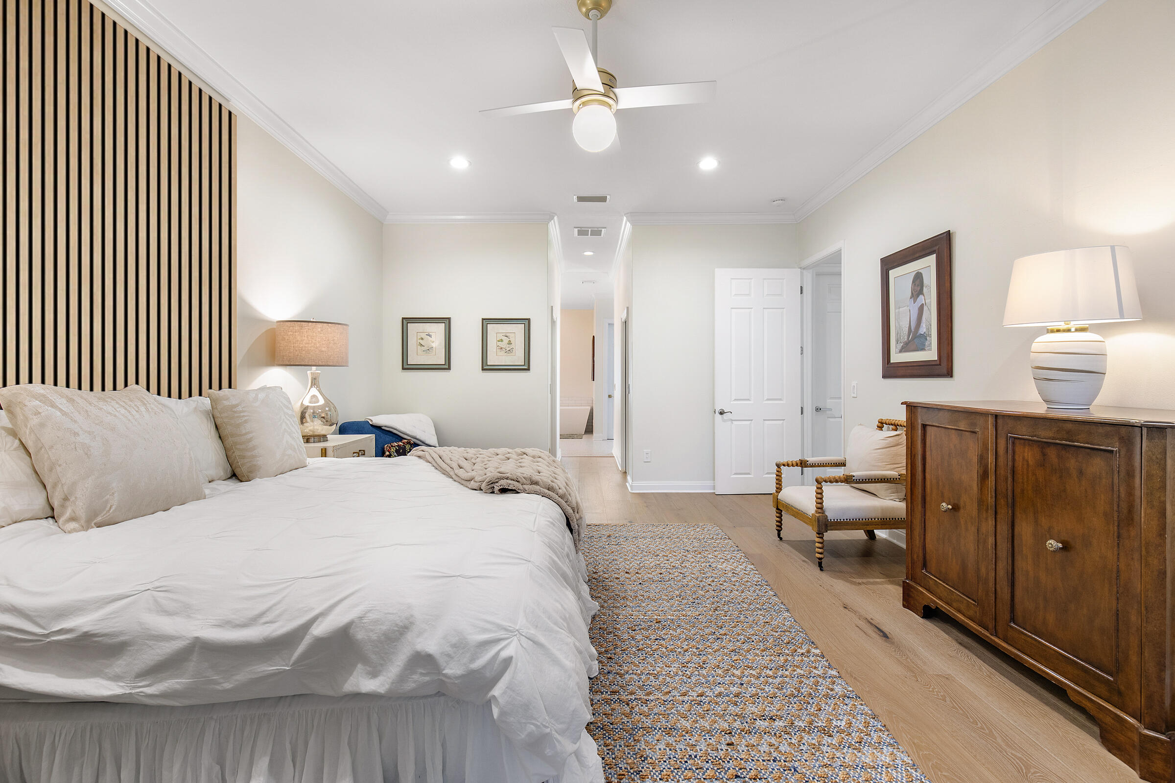 Furnished bedroom with a white bed, striped accent wall, patterned rug, and wooden cabinet.