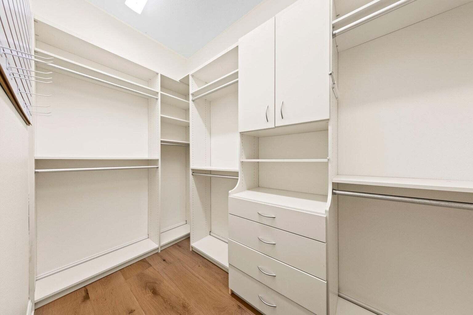 Walk-in closet with white built-in shelving, drawers, and wood flooring.
