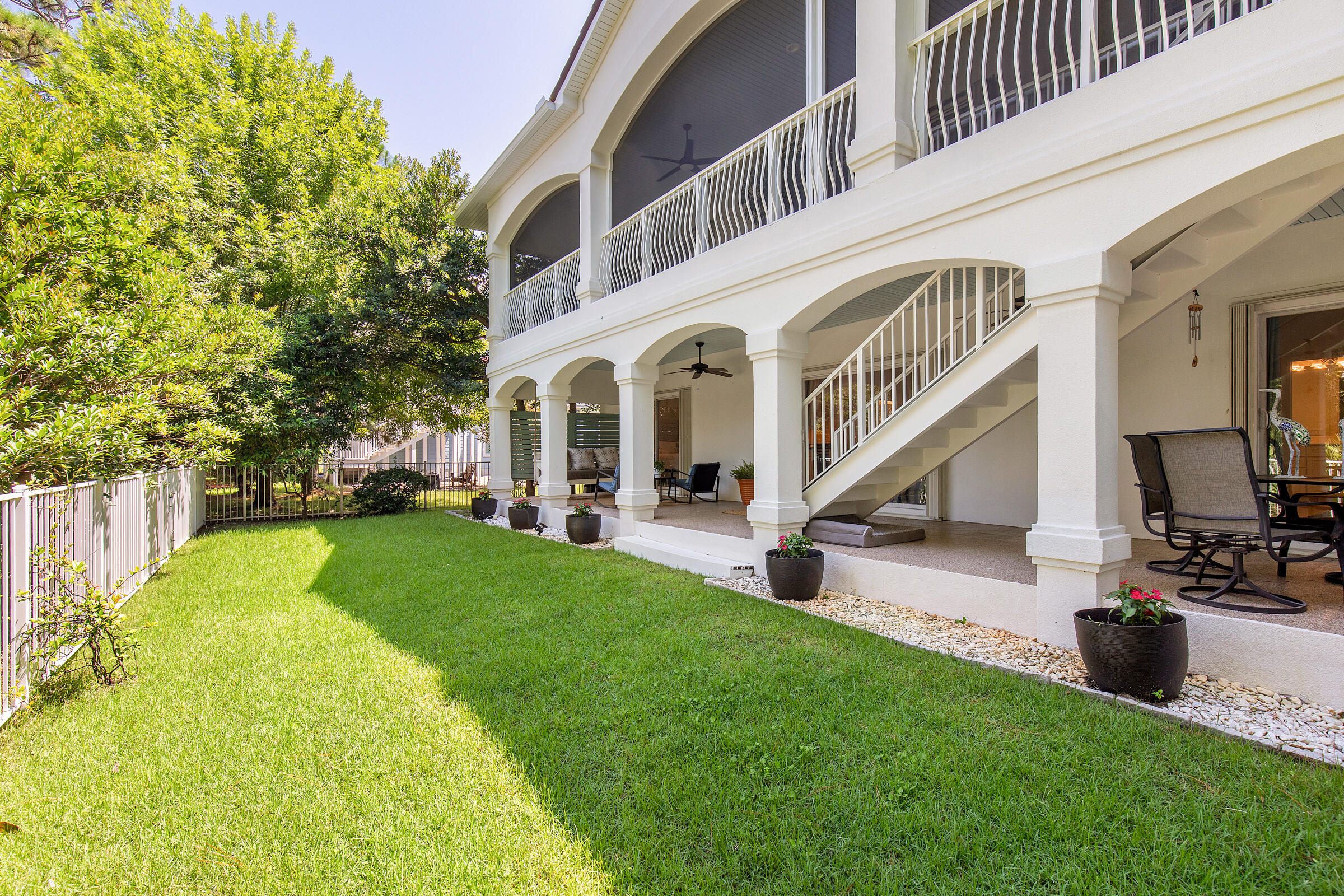 White multi-level home with covered patios and exterior stairs beside a fenced lawn.