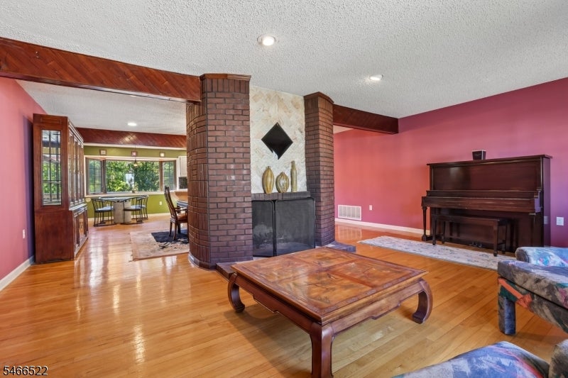 Living room with a brick fireplace, polished hardwood floors, and an upright piano.