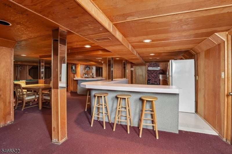 Wood-paneled basement recreation room with a long counter, three stools, and a dining area.