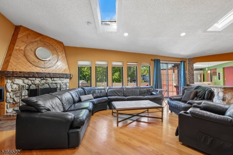 Living room with black leather seating, a stone fireplace, hardwood floors, and skylights.