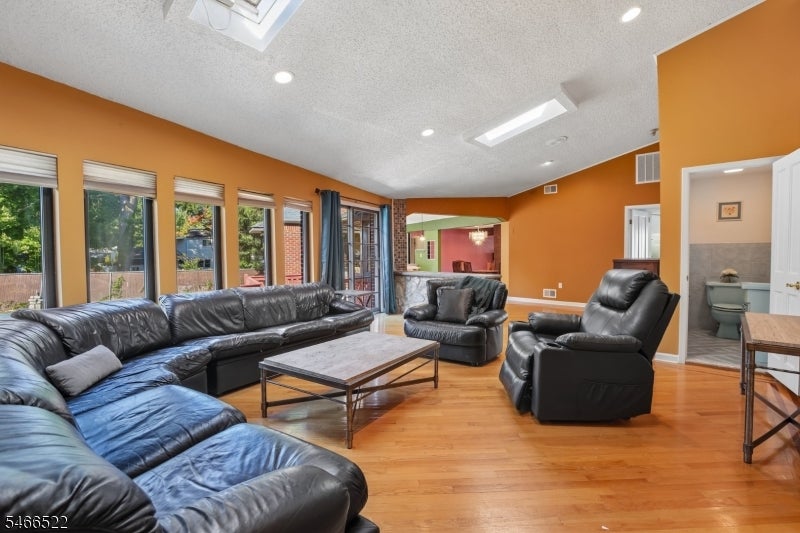 Living room with a black leather sectional, orange walls, hardwood floors, and a skylight.