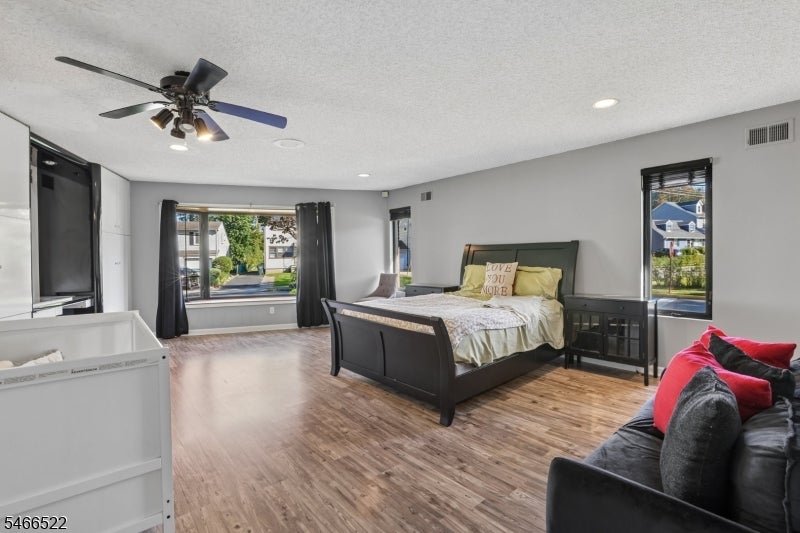 Spacious bedroom with a dark bed, wood-look floors, large windows, and a sofa with red cushions.