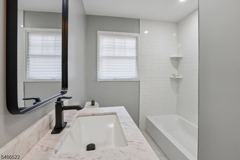 Bathroom with marble-look vanity, black faucet, mirrored cabinet, and white-tiled tub surround.