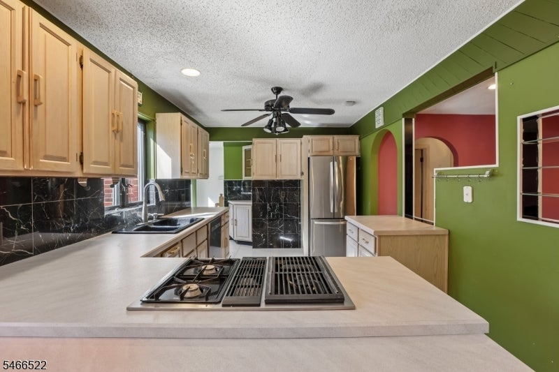 Kitchen with wood cabinets, black stone backsplash, and a large island with a gas cooktop.