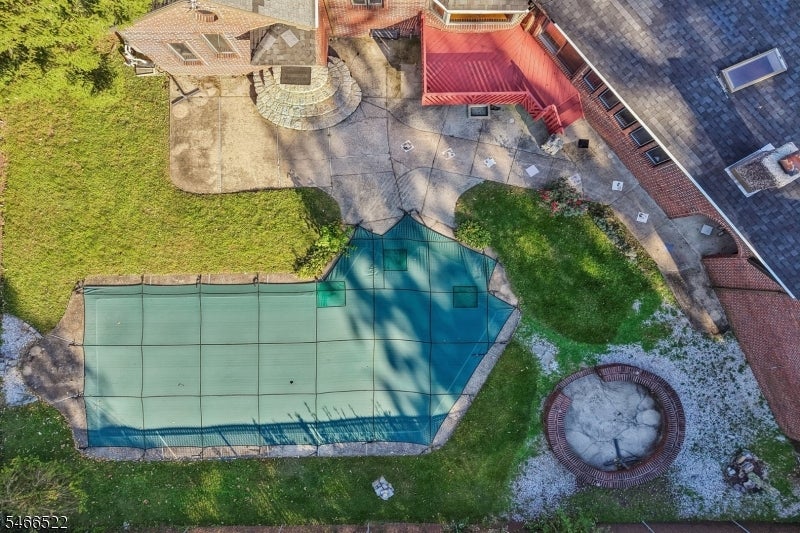 Aerial backyard with a covered pool, paved patio, and circular fire pit.