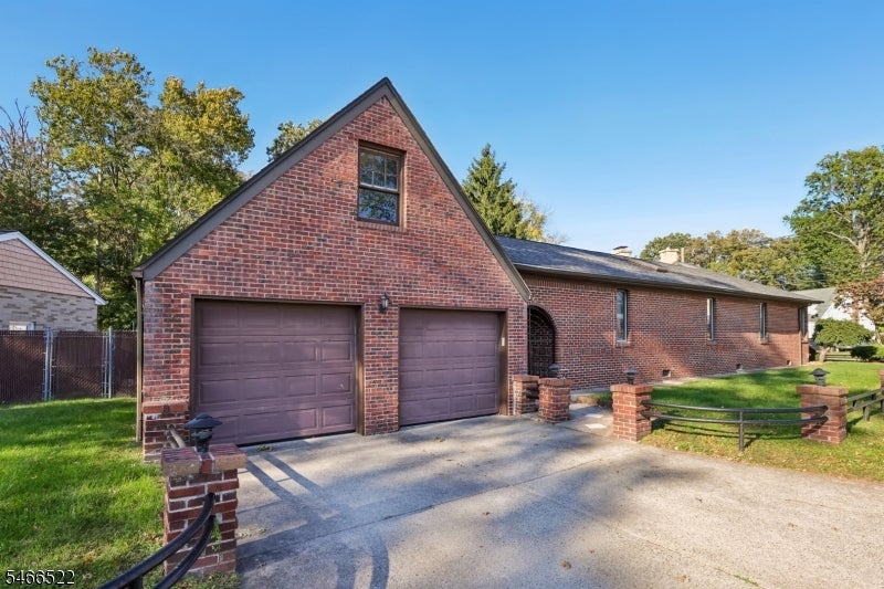 Brick home with a front-facing gable, two garage doors, wide driveway, and fenced lawn.