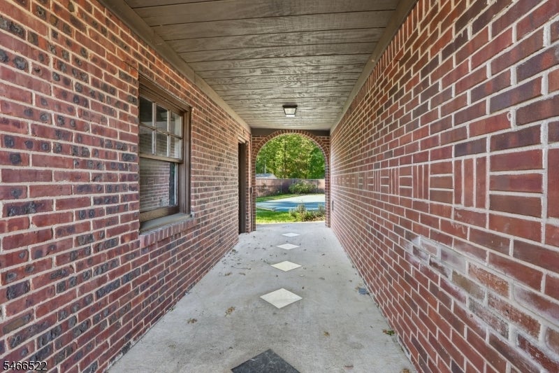Covered brick entry passage with diamond floor inlays leading toward a backyard pool.