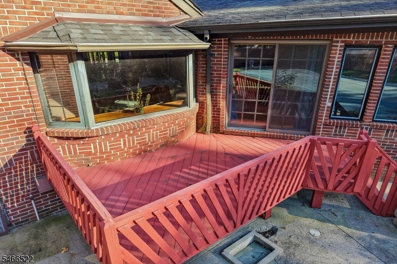 Raised red deck with wooden railings beside a brick house’s bay window and sliding glass door.