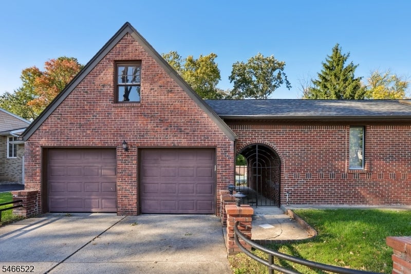 Red-brick home with two garage doors and an arched gated entry walkway.