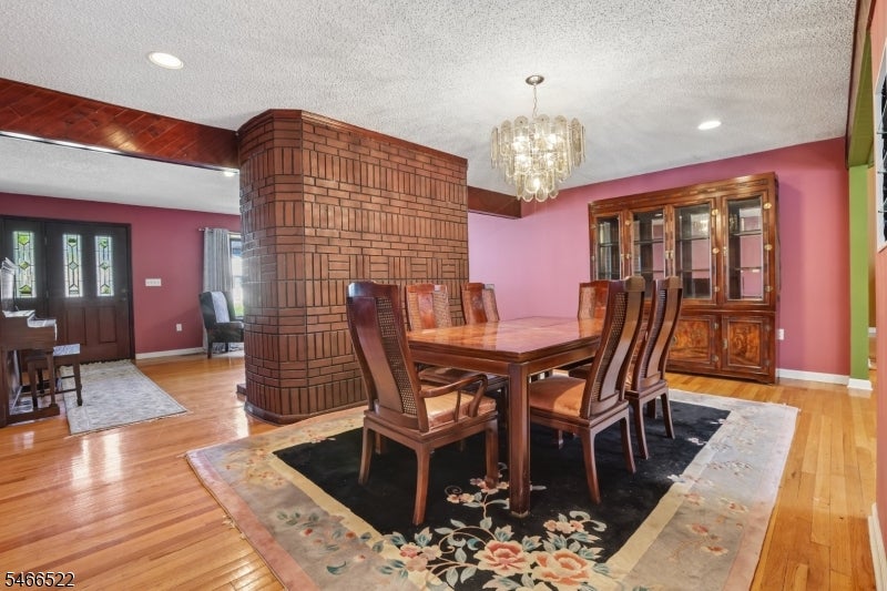 Dining room with a brick fireplace column, wooden table, floral rug, and crystal chandelier.