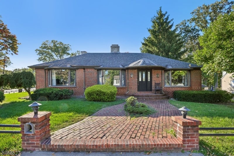Single-story brick house with a central entry, landscaped lawn, and brick walkway.