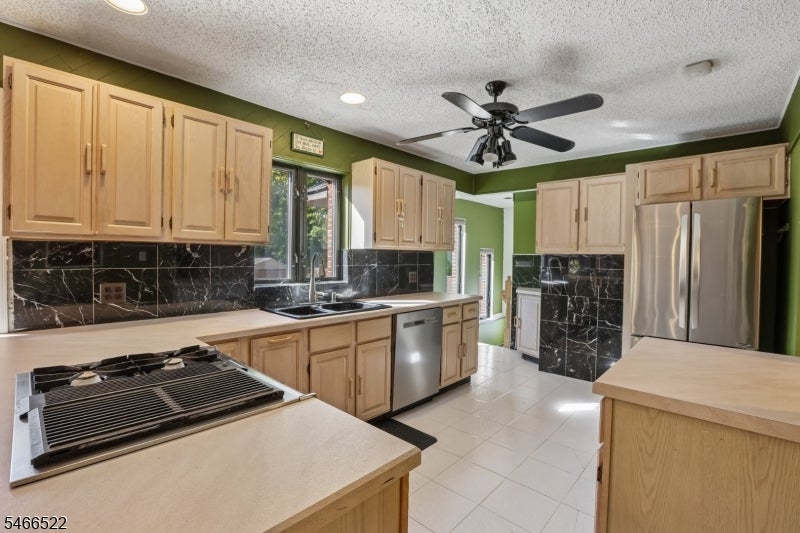Kitchen with light wood cabinets, black backsplash, stainless steel appliances, and broad pale countertops.