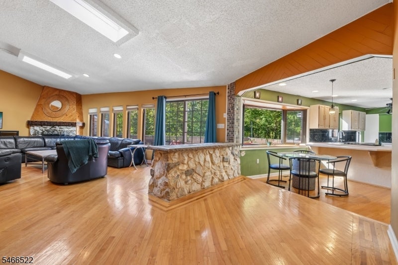 Open-plan living and dining area with hardwood floors, a stone breakfast bar, and large windows.