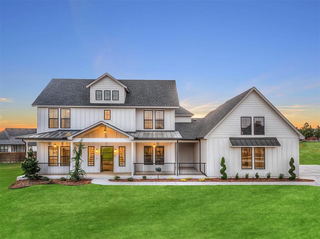 White two-story farmhouse with a covered porch and broad lawn at sunset.