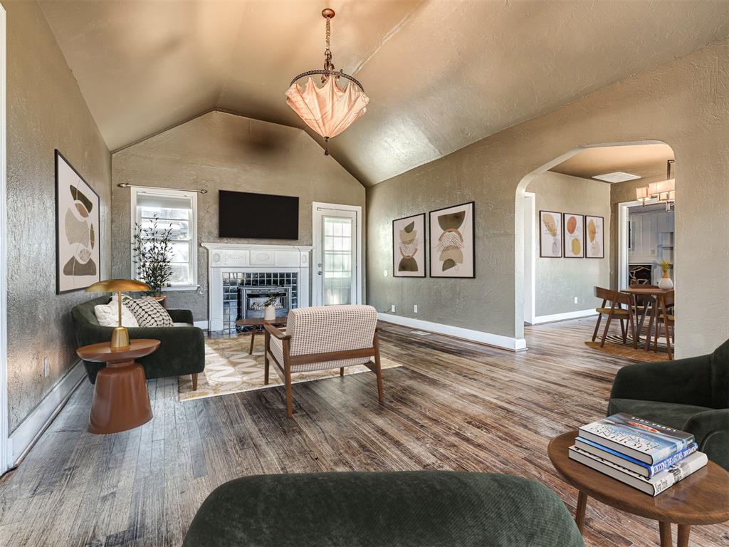 Staged living room with a vaulted ceiling, white fireplace, dark sofas, and an arched opening to the dining area.