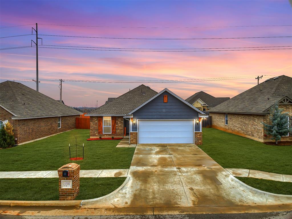 Single-story home with a two-car garage and wide driveway beneath a colorful dusk sky.