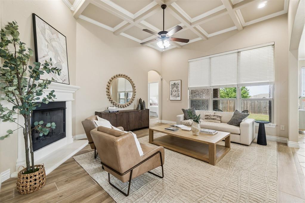 Living room with a coffered ceiling, fireplace, and large windows overlooking a fenced backyard.