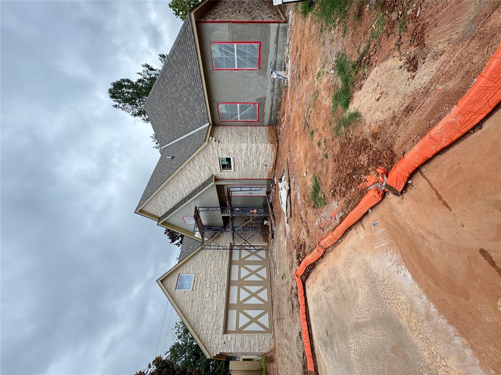 Stone-front house under construction with entrance scaffolding and an unfinished dirt yard.
