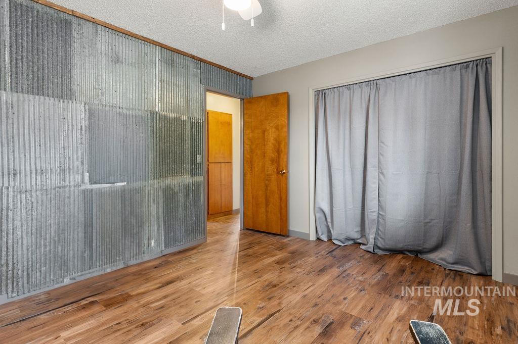Mostly empty room with wood floors, a corrugated metal accent wall, and gray curtains.