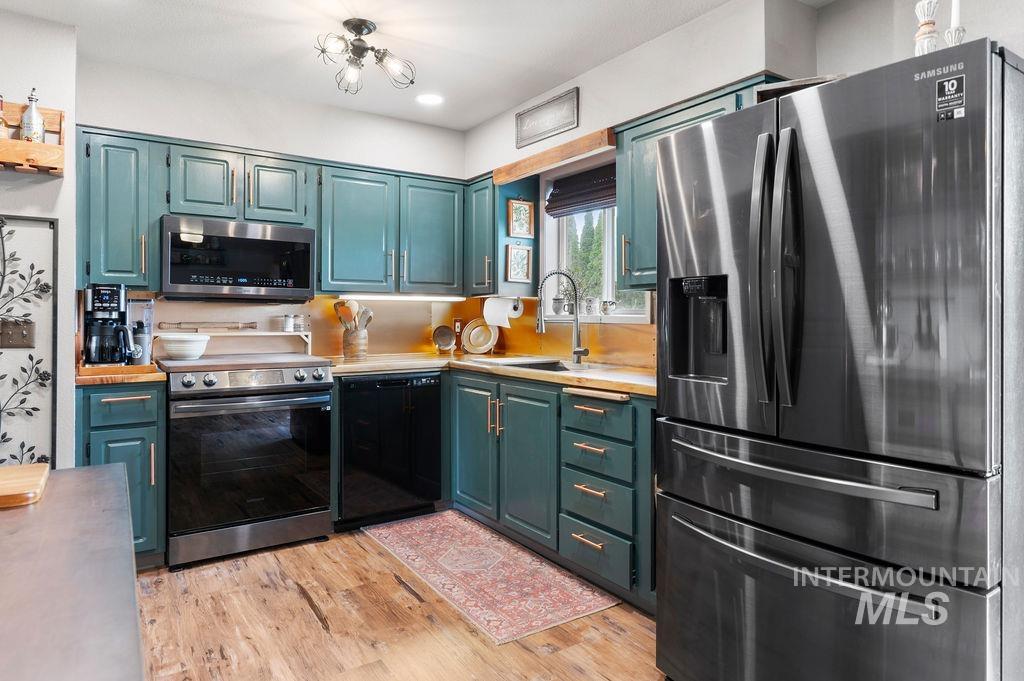 Kitchen with teal-green cabinets, stainless steel appliances, wood countertops, and a patterned floor runner.