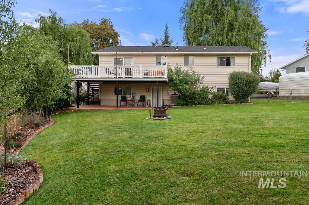 Rear of a beige split-level home with a raised deck, covered patio, and lawn fire pit.