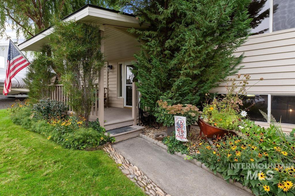 Beige-sided home entrance with a covered porch, flower beds, and an American flag.