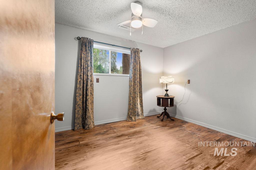Bedroom with wood-look flooring, patterned curtains, a ceiling fan, and a small table with a lamp.