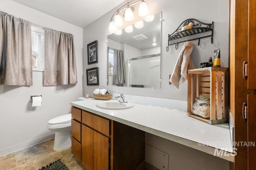 Bathroom with a long white countertop, wooden vanity, and large mirror beside a curtained window.