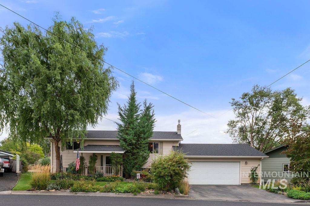 Beige home with a broad attached garage, landscaped front yard, and mature trees.