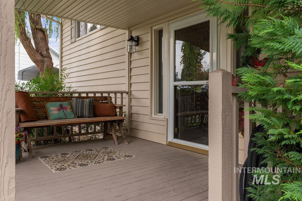 Covered porch with a wooden bench, colorful cushions, and a patterned rug beside the glass entry door.