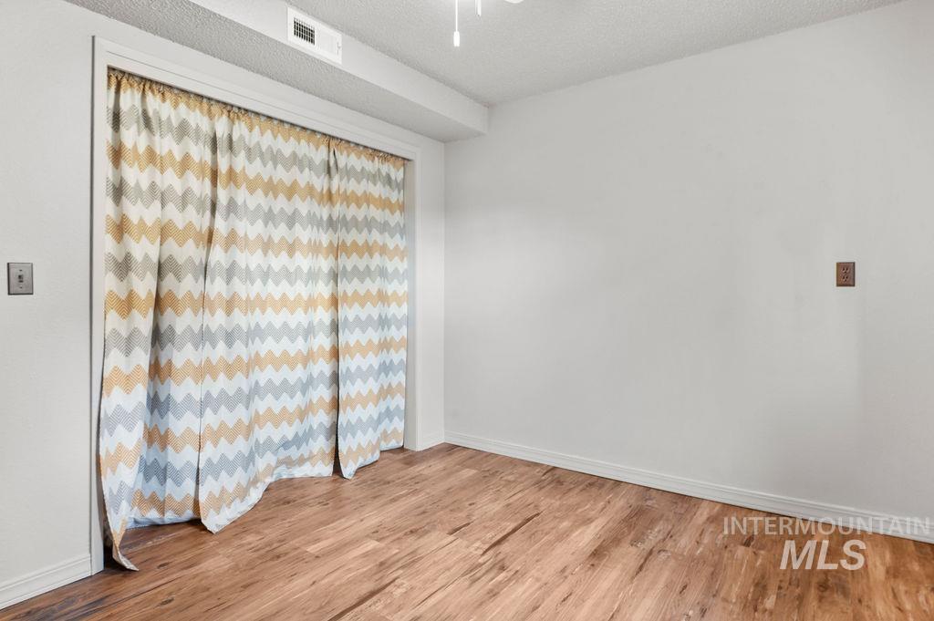 Empty room with wood-look flooring and patterned curtains covering a wide opening.