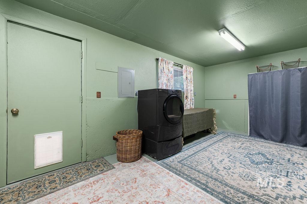 Laundry room with a black washer and dryer, curtained window, patterned rugs, and a fabric-covered table.